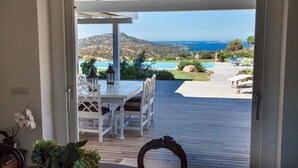 Une terrasse extérieure avec une table et des chaises, une vue sur une piscine et des montagnes, et un ciel dégagé.