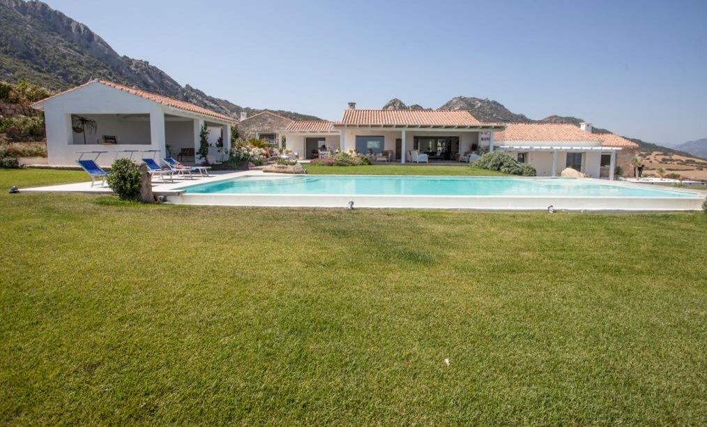 A modern villa with a swimming pool, outdoor seating, and a mountainous backdrop.