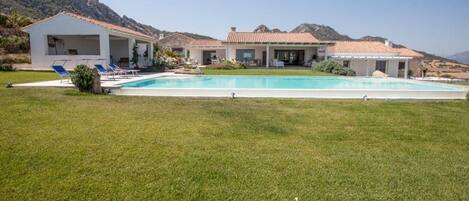 A modern villa with a swimming pool, outdoor seating, and a mountainous backdrop.