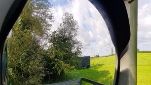 A round mirror reflecting a grassy area with a bench and a trailer. - Glamping Thorpe (Banbury)