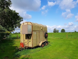 A vintage trailer with a small attached structure, parked in a grassy field.