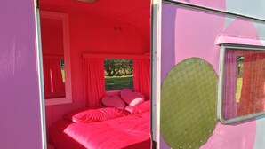 A pink room with a bed, curtains, and a window. - Glamping Thorpe (Banbury)