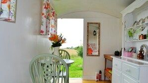 A cozy kitchen with a dining table, chairs, a white cabinet with dishes, and a mirror on the wall. - Glamping Thorpe (Banbury)