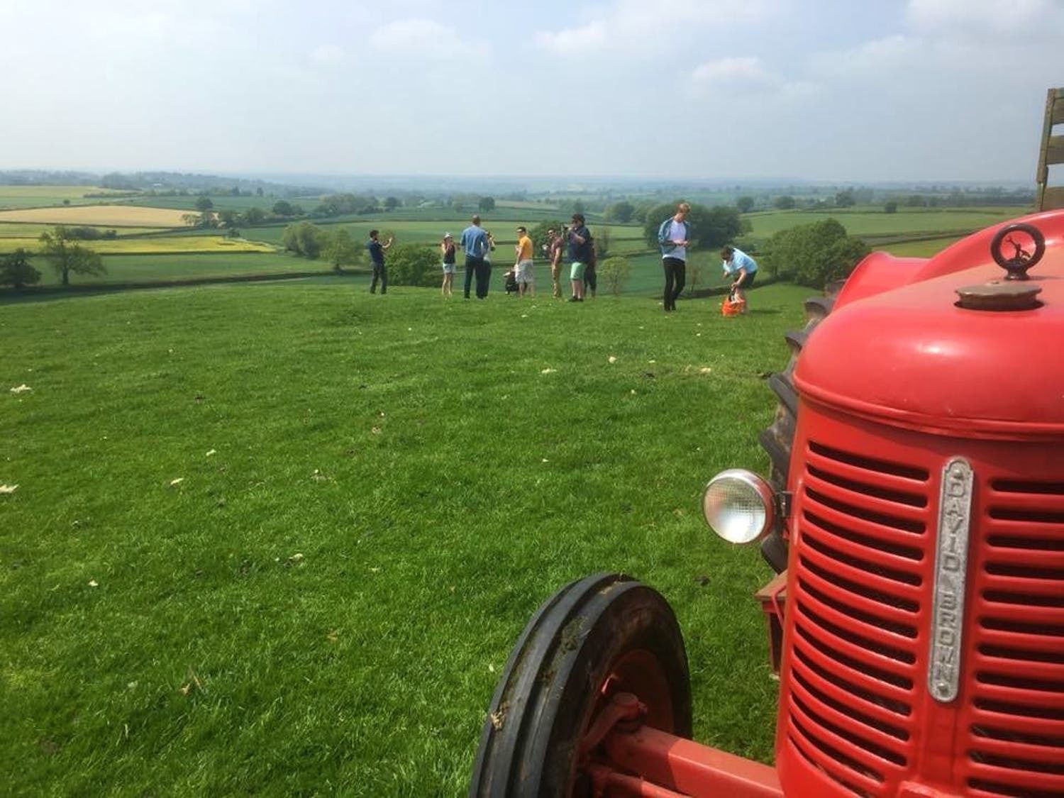 A red tractor with the text "DAD BROWN" on the front, parked on a grassy field with a group of people in the background.