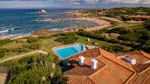 Ein Küstenanwesen mit Schwimmbad, Gebäuden mit Terrakotta-Dachziegeln und Blick auf Meer und Strand.