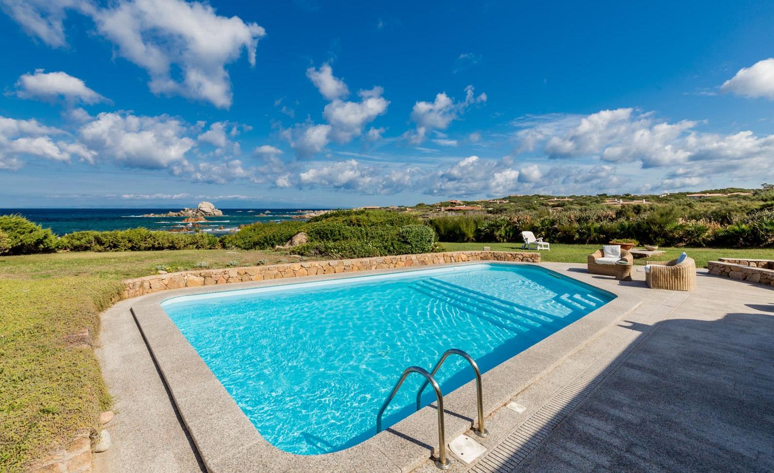 A rectangular swimming pool with a clear blue water surface, surrounded by a stone wall and a grassy area.
