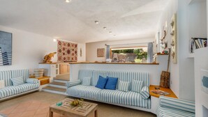 Ein gemütliches Wohnzimmer mit einem gestreiften Sofa, einem Holztisch und Blick auf den Garten durch ein Fenster.