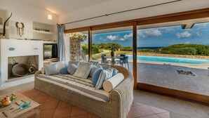 Ein geräumiges Wohnzimmer mit einer großen Couch, einem Kamin und Blick auf Pool und Landschaft.