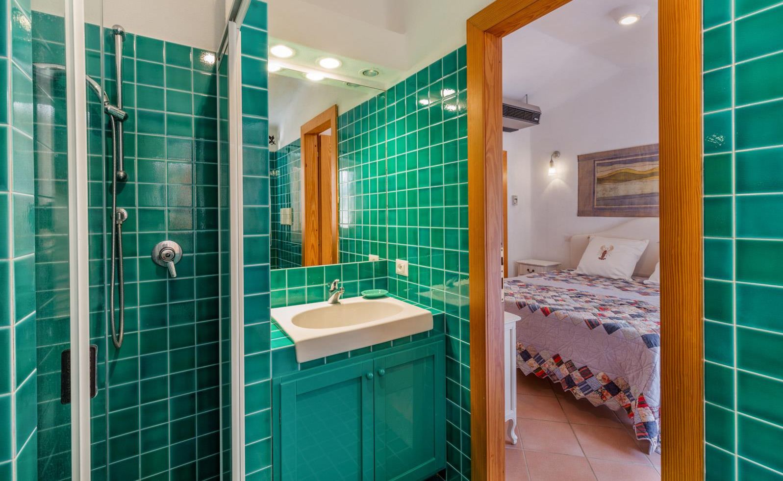 Un baño con azulejos verdes, un lavamanos y una ducha.