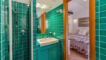 Un baño con azulejos verdes, un lavamanos y una ducha.