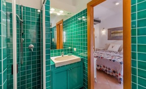 Un baño con azulejos verdes, un lavamanos y una ducha.