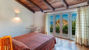A bedroom with a bed, a chair, a shelf, and a view through a glass door.