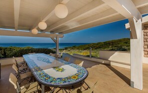 An outdoor patio with a table and chairs, overlooking a scenic view of the sea and hills. - Villa La Bitta (Badesi)