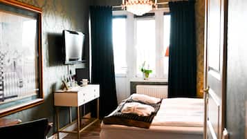 Habitación de hotel con piso de madera, una cama, un escritorio con televisor y un candelabro.