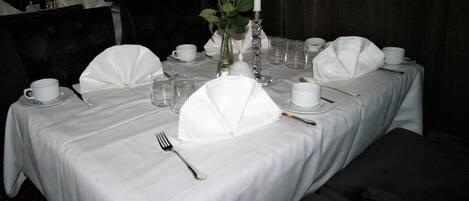 Mesa dispuesta para una cena formal, con manteles y servilletas blancas, y un centro de mesa con velas.
