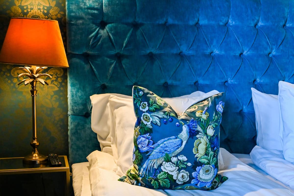 A bedroom with a tufted blue headboard, white bedding, and a floral pillow.