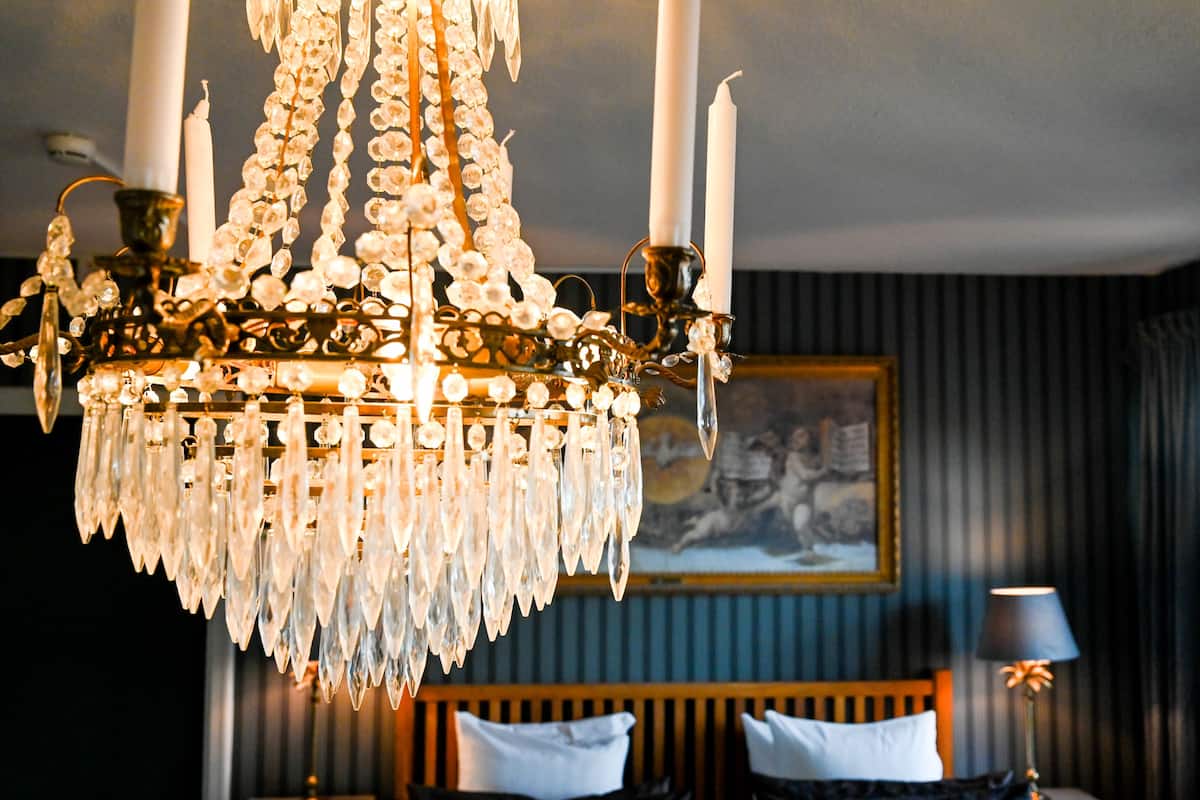 A chandelier with multiple candles, a bed with white pillows, and a painting on the wall.