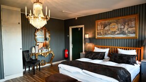 A hotel room with a large bed, a chandelier, a vanity with a mirror, and a painting on the wall. - Palace Hotell (Hultsfred)