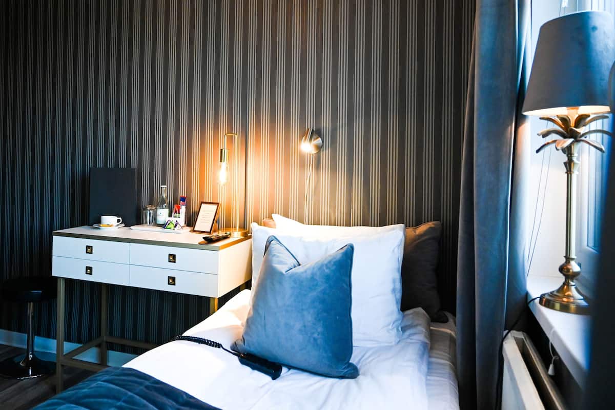 A hotel room with a bed, bedside table, lamp, and a wall-mounted light fixture.