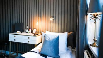 Una habitación de hotel con cama, mesita de noche, lámpara y una pared a rayas verticales.