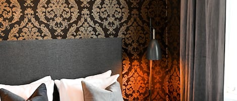 A neatly made bed with a dark headboard and white bedding, a chandelier, and patterned wallpaper.