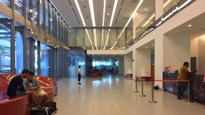 A spacious lobby with a modern design, featuring a glass facade, a seating area with red chairs, and a reception desk.