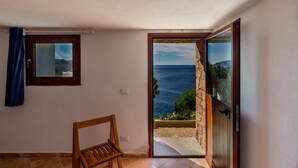 A room with a view of the sea, a wooden chair, and a stone wall. - Villa Saluto del Sole (Trinità d'Agultu e Vignola)
