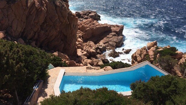 A swimming pool surrounded by rocky cliffs and ocean waves. - Villa Saluto del Sole (Trinità d'Agultu e Vignola)