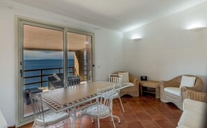 A balcony with a view of the sea, a dining table with chairs, and wicker furniture. - Villa Saluto del Sole (Trinità d'Agultu e Vignola)