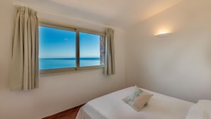 A bedroom with a bed, a window with curtains, and a view of the sea. - Villa Saluto del Sole (Trinità d'Agultu e Vignola)