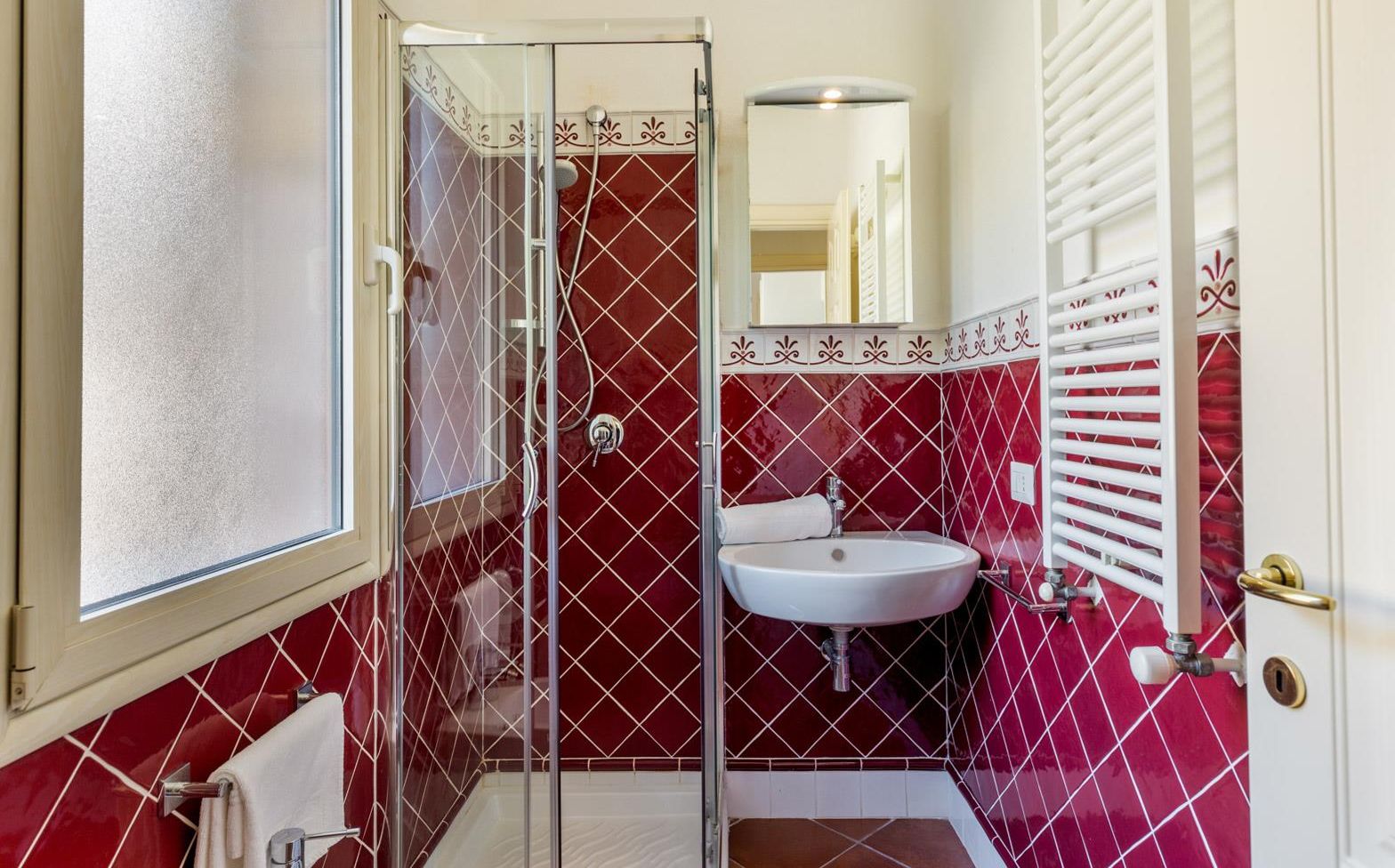 A bathroom with a glass shower enclosure, a white sink, and a red-tiled wall.