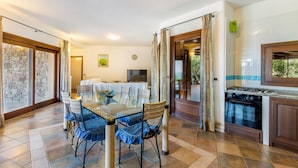 Un coin repas avec une table et des chaises en verre, un téléviseur et une cuisine équipée d’une cuisinière.