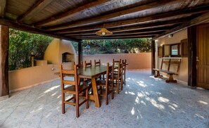 Un patio al aire libre con una mesa redonda y sillas, piso de baldosas de piedra y techo de madera.