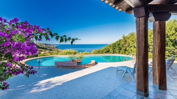Une piscine à bord incurvé, entourée d’une terrasse carrelée et de chaises longues.