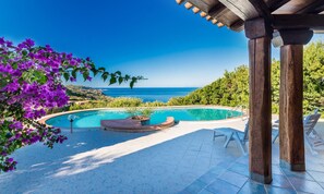 A swimming pool with a curved edge, surrounded by a tiled patio and lounge chairs. - Villa Sa Laddera (Trinità d'Agultu e Vignola)