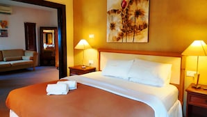 Una habitación de hotel con una cama grande, dos lámparas de noche, un cuadro en la pared y un sofá en la habitación contigua.