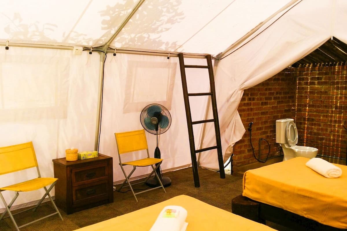 A tented room with two beds, a fan, a ladder, and a small table with a chair.