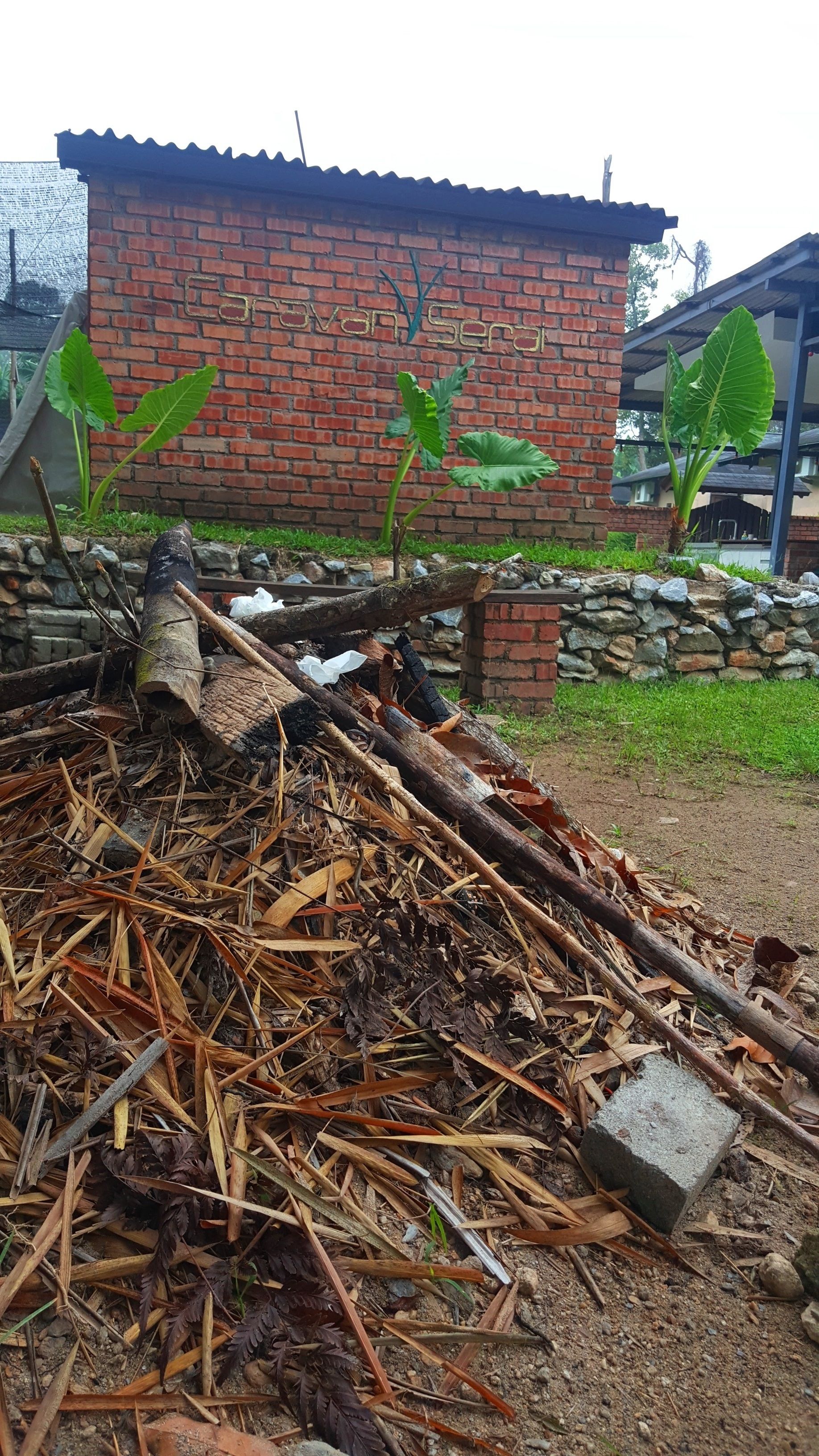 A pile of wood and debris in front of a brick building with a metal roof.