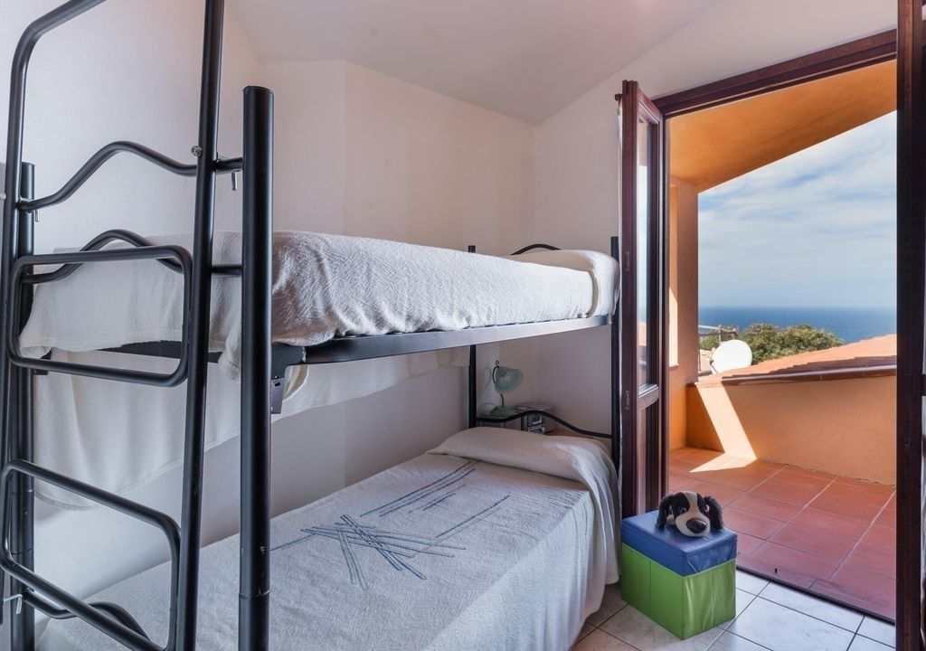Ein Schlafsaalzimmer mit Etagenbetten, einem kleinen Schreibtisch und Meerblick durch eine offene Tür.
