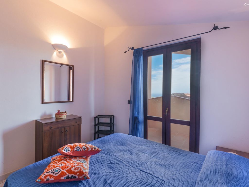 Une chambre à coucher comprenant un lit, une commode, un miroir et une vue sur l’extérieur, accessible par une porte-fenêtre coulissante.
