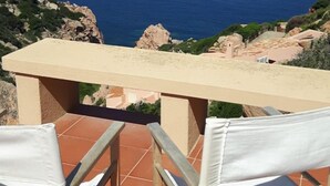A terrace with two white cushioned chairs and a table, overlooking a coastal view with the sea and rocky landscape. - Villetta Ambra Rossa (Trinità d'Agultu e Vignola)