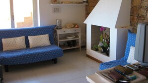 A living room with a blue sofa, a white fireplace, and a stone wall. - Villetta Ambra Rossa (Trinità d'Agultu e Vignola)