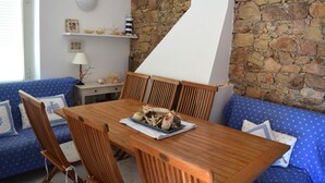 A dining area with a wooden table, blue upholstered sofa, and a stone wall. - Villetta Ambra Rossa (Trinità d'Agultu e Vignola)