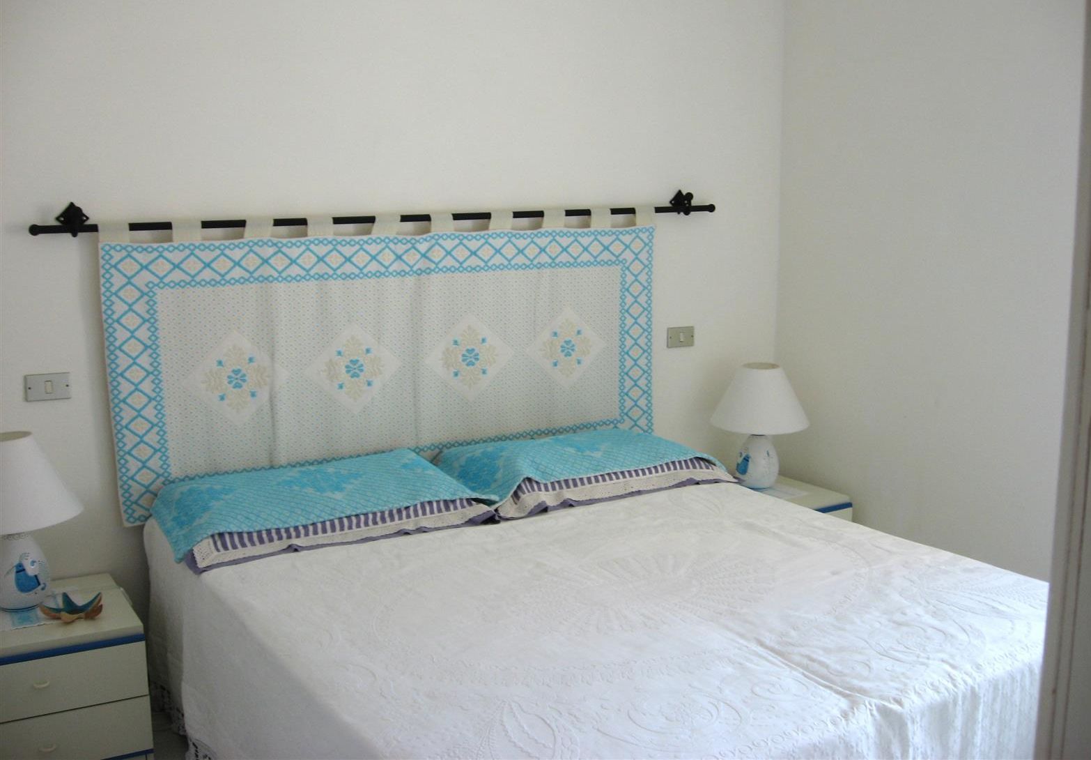 A bed with a patterned headboard, two pillows, and a bedside table with a lamp.