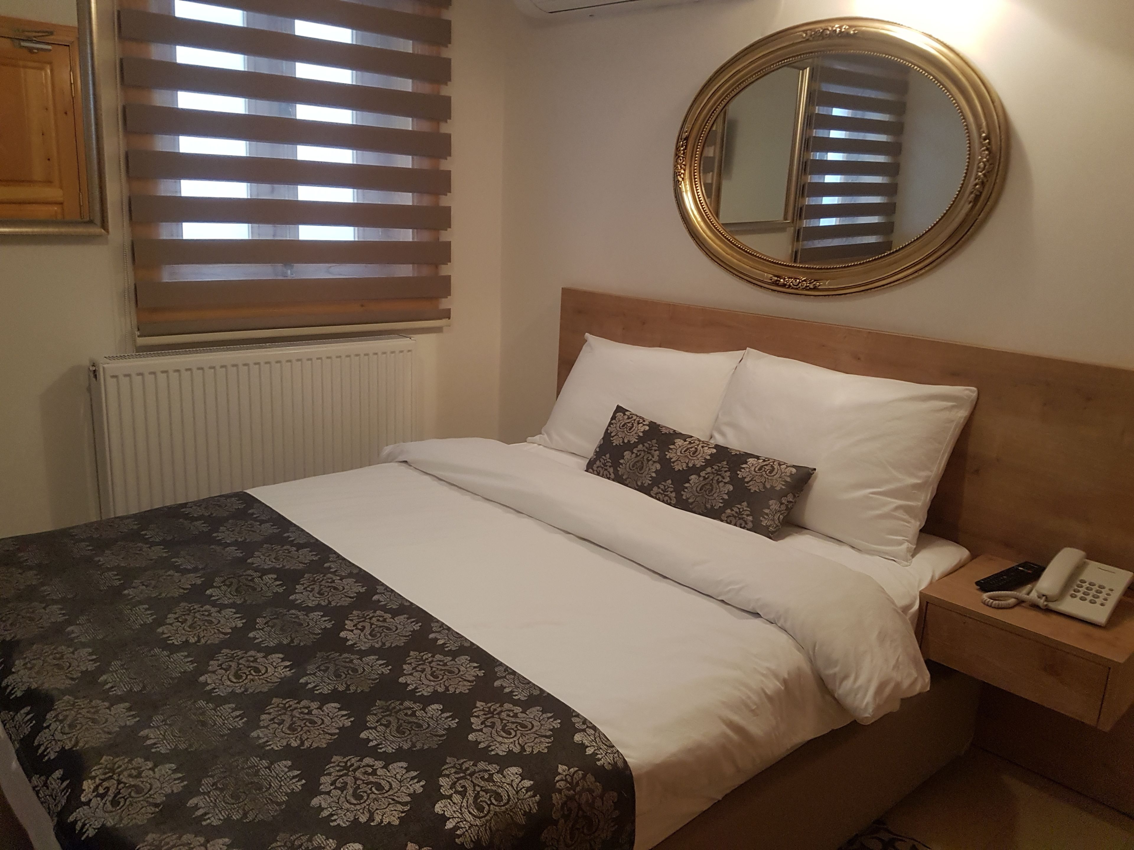 A neatly made bed with a patterned bedspread, a bedside table with a phone, and a round mirror on the wall.