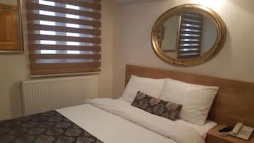 Un lit bien fait, recouvert d’une couvre-lit à motifs, une table de chevet avec un téléphone et un miroir rond accroché au mur.