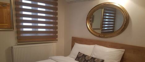 A neatly made bed with a patterned bedspread, a bedside table with a phone, and a round mirror on the wall.