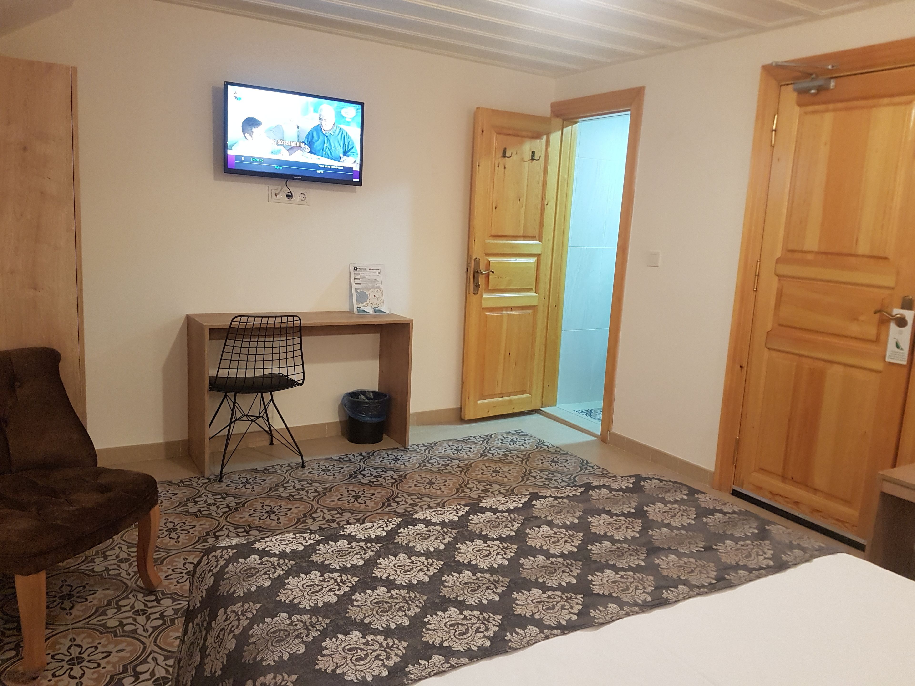 Una habitación de hotel con una cama, un escritorio con silla, televisión y una puerta de madera.