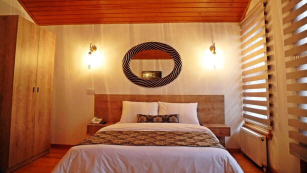 A bedroom with a wooden ceiling, a bed with white bedding, a bedside table with a lamp, and a circular mirror on the wall. - Belizia Hotel (Istanbul)