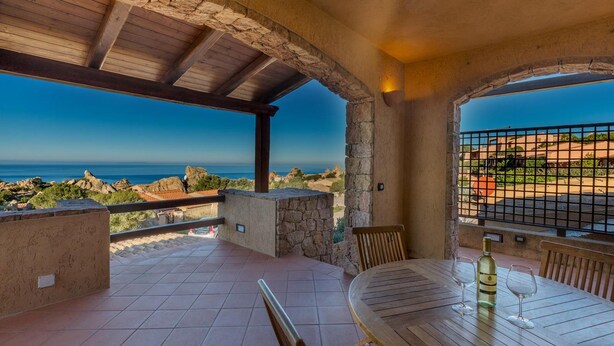 Eine Terrasse mit Tisch und Stühlen, einer Weinflasche und Blick auf das Meer und die felsige Landschaft.